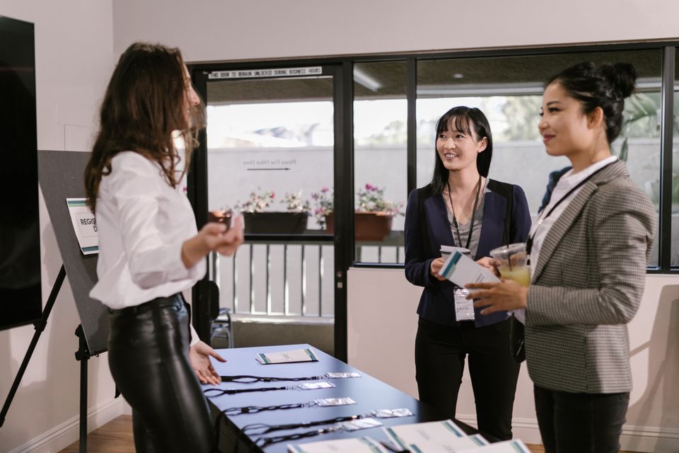 Professionals talk beside a welcome table at an event.