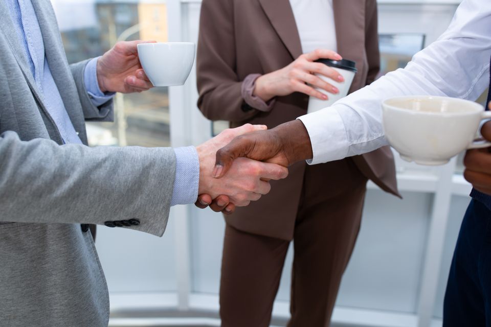 Two people holding coffee cups shake hands.