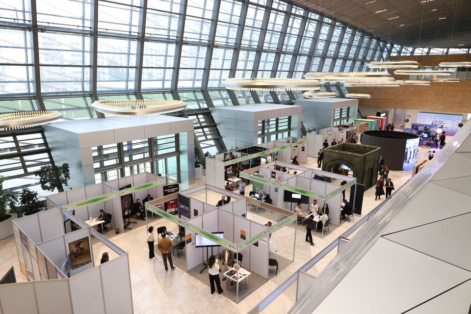 An exhibition hall seen from above, with rows of booths and visitors walking between them.