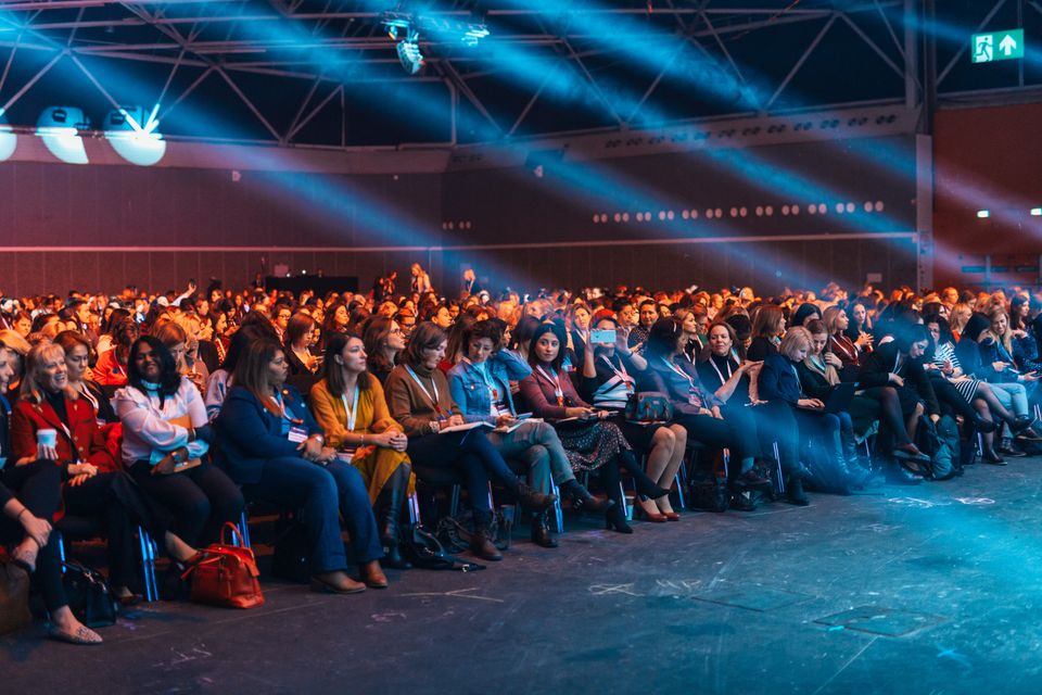A large conference audience seated under blue stage lighting.