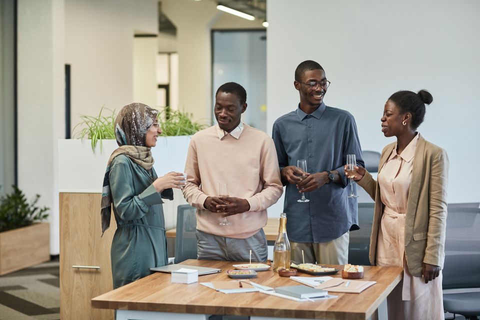 Four professionals hold drinks and talk around a table at a reception.