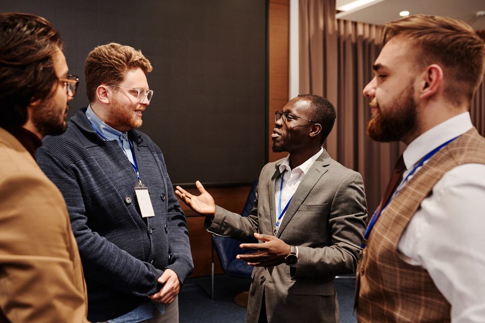 Professionals wearing name badges talk while standing at an event.